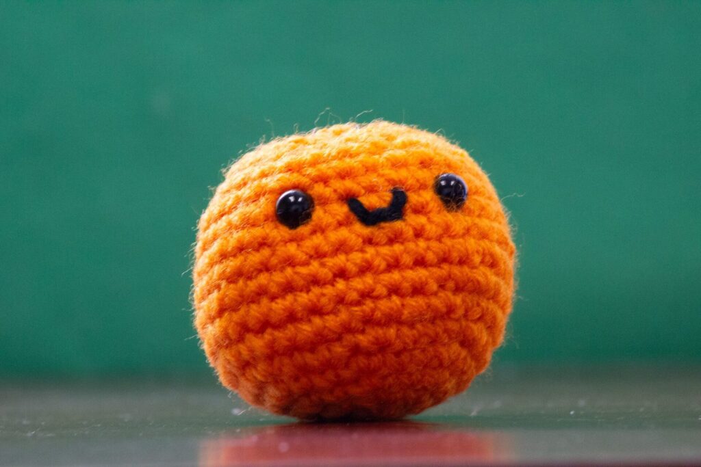 Gehäkelte orangefarbene Amigurumi-Kugel mit aufgesticktem Lächeln