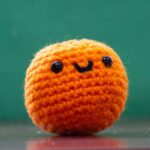Gehäkelte orangefarbene Amigurumi-Kugel mit aufgesticktem Lächeln