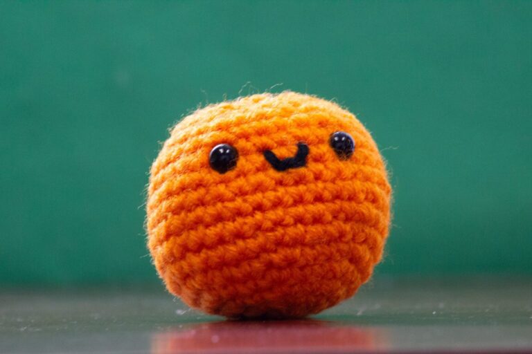 Gehäkelte orangefarbene Amigurumi-Kugel mit aufgesticktem Lächeln