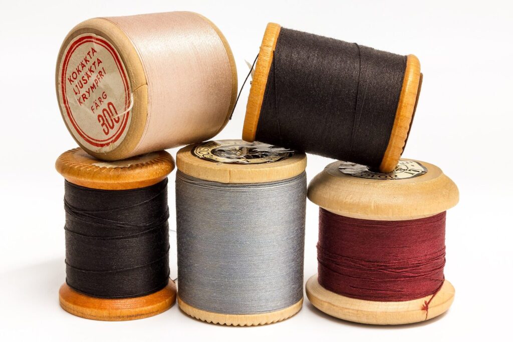 Garnrollen aus Holz mit Nähgarn in Beige, Rot, Grau und Schwarz