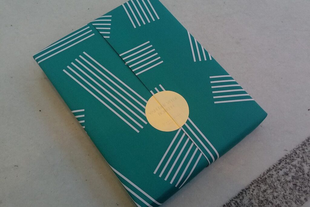 In grünes Papier mit weißen Streifen eingepacktes Geschenk mit goldenem Aufkleber
