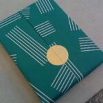 In grünes Papier mit weißen Streifen eingepacktes Geschenk mit goldenem Aufkleber
