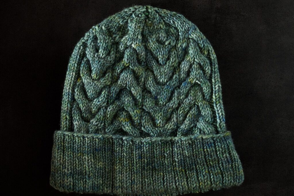 Grün melierte, handgestrickte Mütze mit Zopfmuster und Umschlag