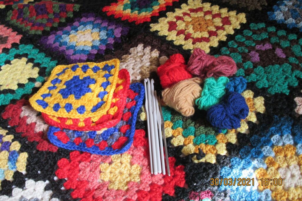 Bunte Granny Squares mit Häkelnadeln auf einer Häkeldecke