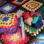 Bunte Granny Squares mit Häkelnadeln auf einer Häkeldecke
