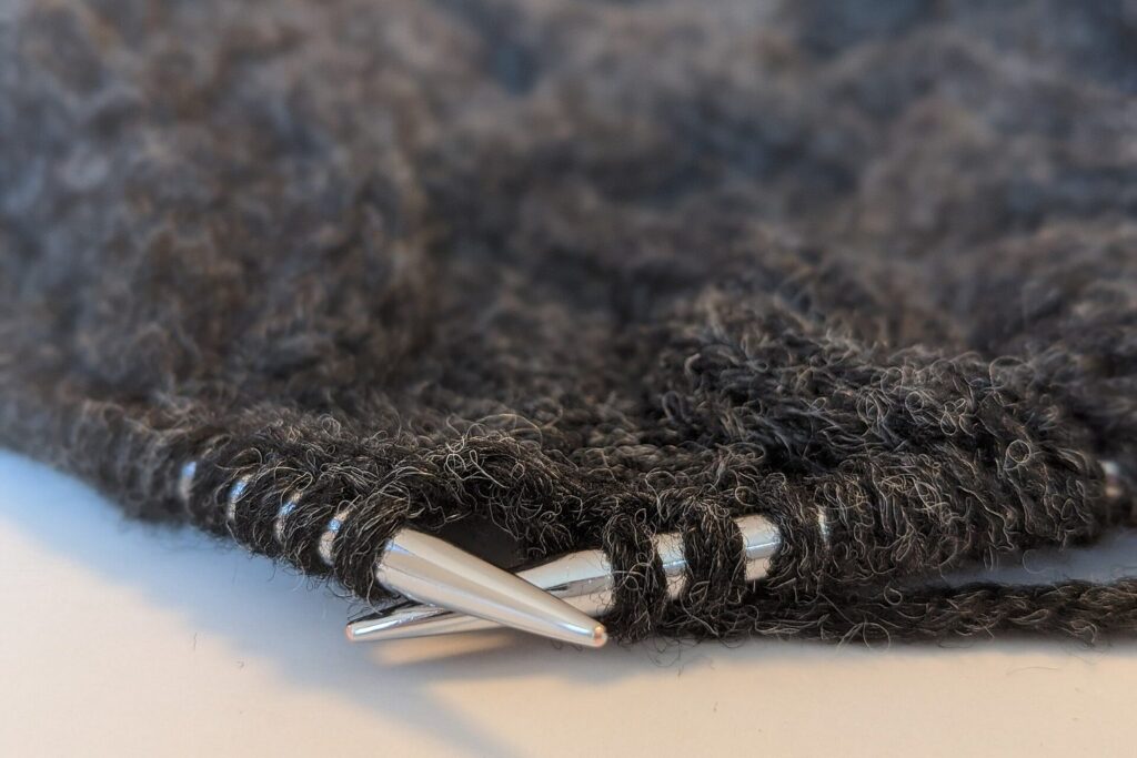 Graue Wolle mit Metallstricknadeln und einem angefangenen Strickstück