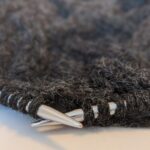 Graue Wolle mit Metallstricknadeln und einem angefangenen Strickstück