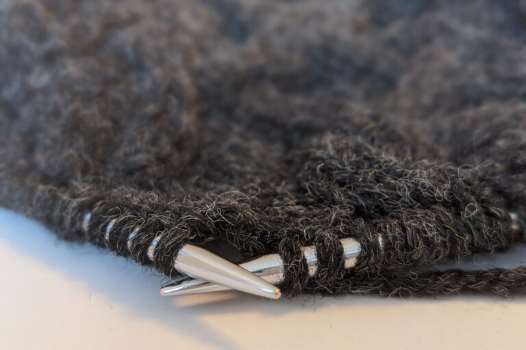 Graue Wolle mit Metallstricknadeln und einem angefangenen Strickstück