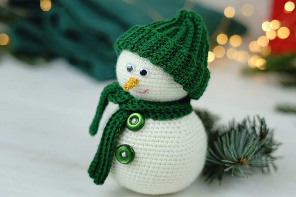 Gehäkelter Schneemann mit Mütze und Schal vor weihnachtlichem Hintergrund