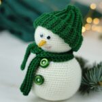 Gehäkelter Schneemann mit Mütze und Schal vor weihnachtlichem Hintergrund