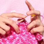 Hände stricken mit Holznadeln an einem pinkfarbenen Strickstück