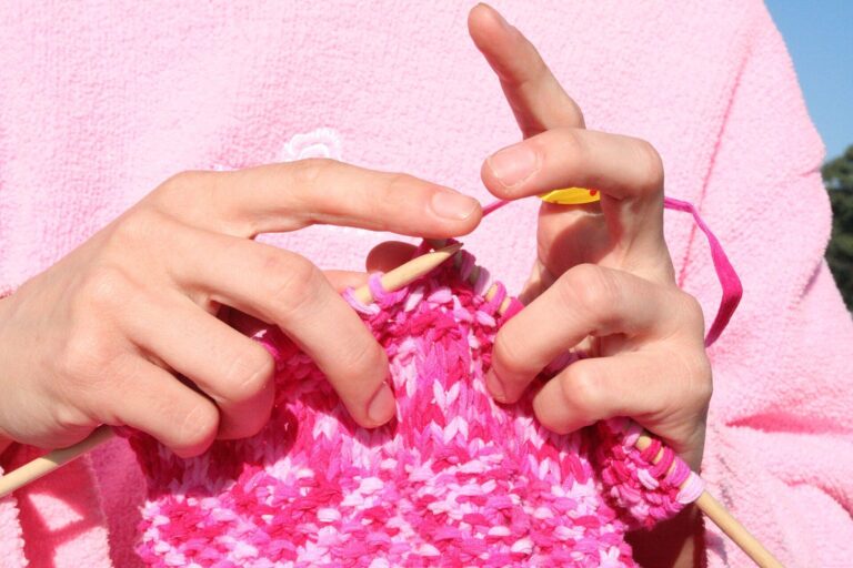 Hände stricken mit Holznadeln an einem pinkfarbenen Strickstück