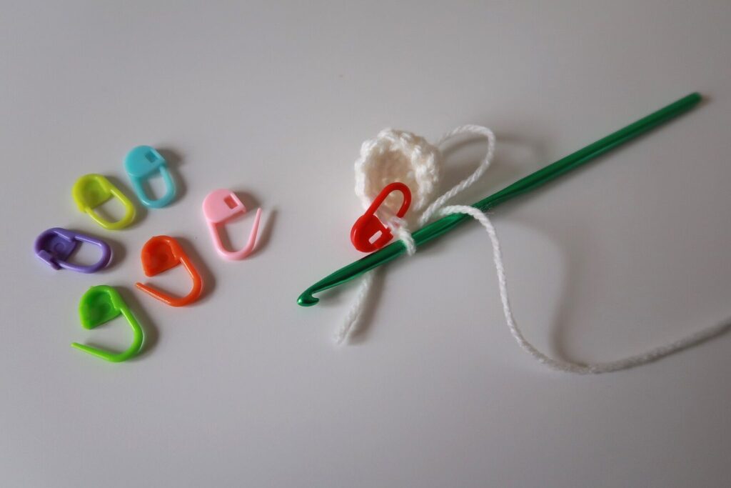 Bunte Maschenmarkierer und eine Häkelnadel auf hellem Untergrund