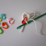 Bunte Maschenmarkierer und eine Häkelnadel auf hellem Untergrund