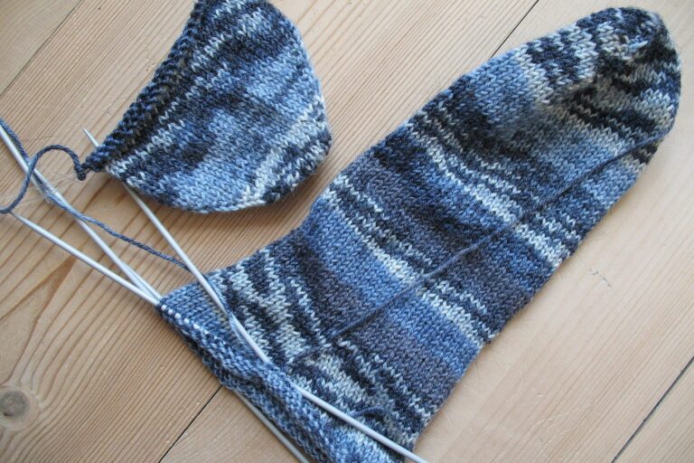 Halbfertige blau melierte Socke auf einem Nadelspiel neben einer fertigen Socke