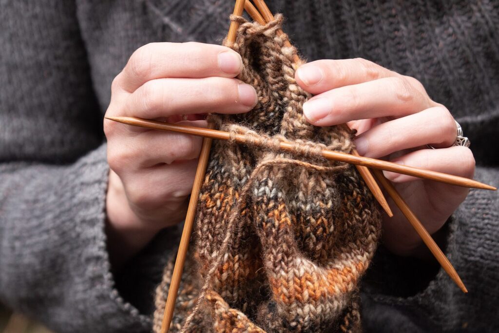 Hände stricken eine Socke aus brauner Wolle mit einem Nadelspiel