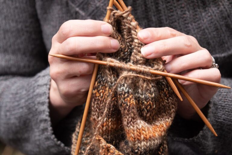 Hände stricken eine Socke aus brauner Wolle mit einem Nadelspiel