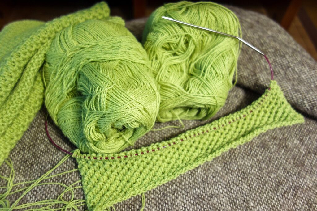 Grüne Merinowolle mit Rundstricknadel und angefangenem Strickstück